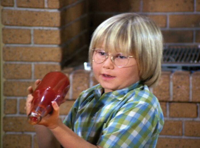 A young boy with glasses shaking a ketchup bottle, an image that reminds you how old you are.