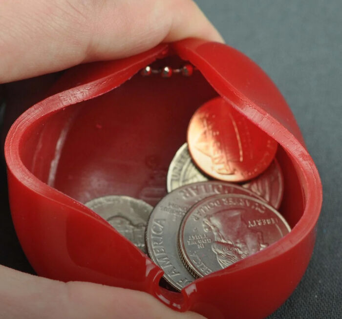 Hand holding a red squeeze coin purse filled with change, reminding you how old you are.