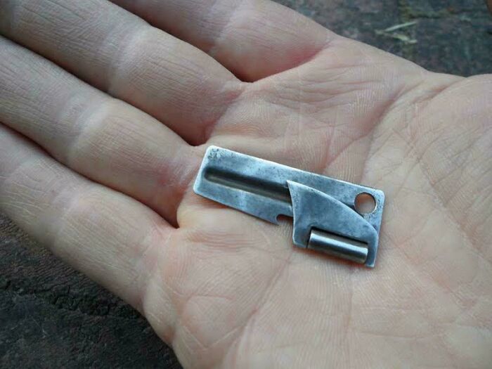 A small, vintage can opener rests in the palm of a hand, a nostalgic item for those who remember it.