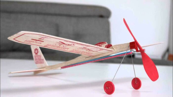 A classic red and white balsa wood model airplane with a propeller and wheels, one of many images that take you way back.