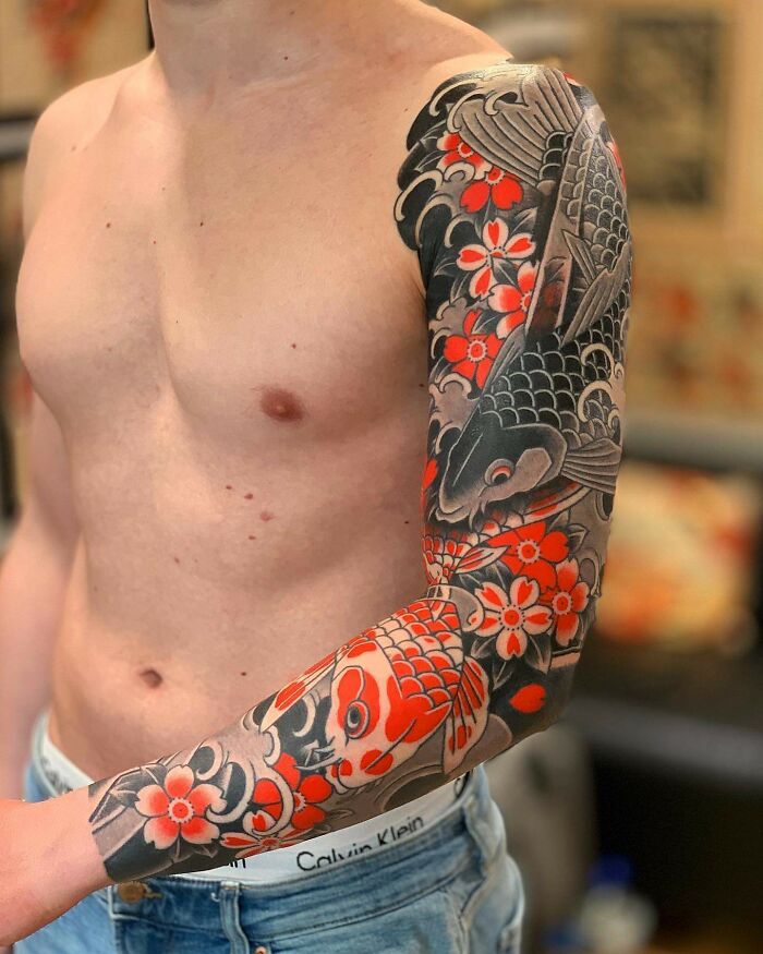 Sleeveless colorful koi fish and floral cool tattoo sleeve on a man's arm, showcasing bold black and red ink designs.