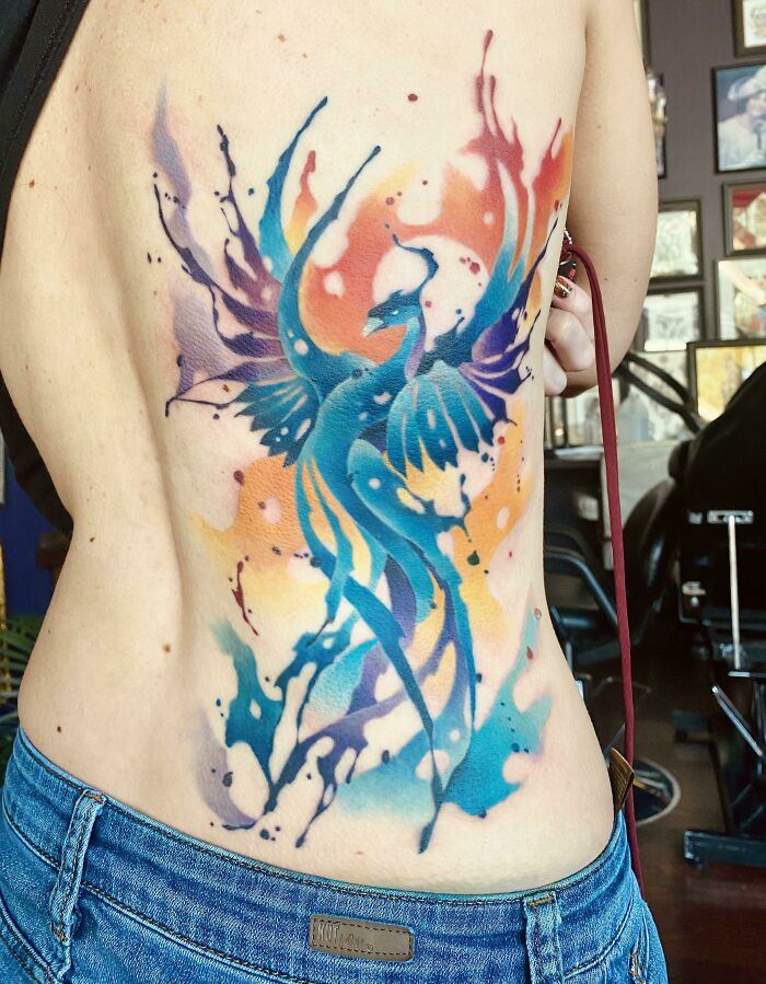 Vibrant watercolor phoenix tattoo on a person's side showcasing cool tattoos with bright blue, orange, and purple hues.