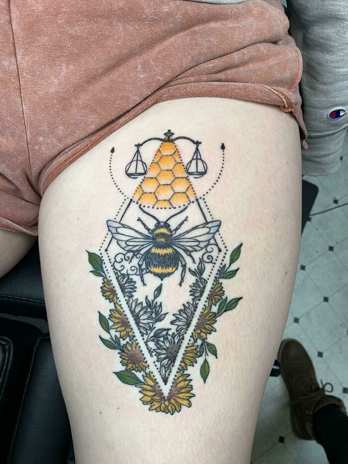 Tattoo of a bee with honeycomb and sunflower design on thigh, showcasing a cool tattoo with detailed linework and color.