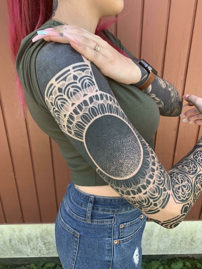 Woman with cool tattoos covering her arm, featuring intricate black ink patterns and dot work designs outdoors.