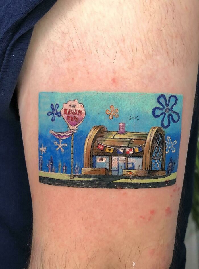 Colorful cool tattoo of a cartoon-style building with flower designs, showcasing creative and unique tattoo art on skin.