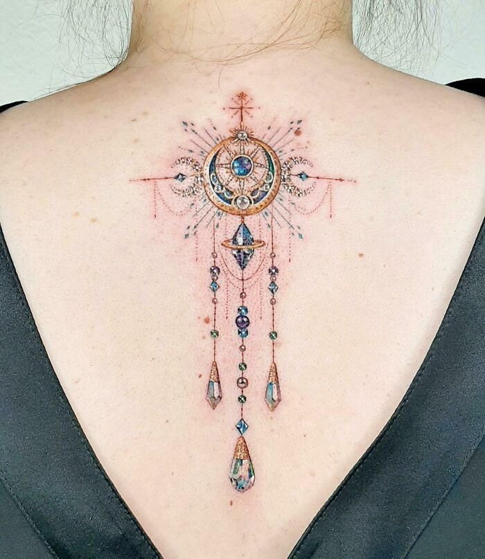 Delicate cool tattoo on upper back featuring intricate geometric shapes and gemstone details with fine linework and shading.