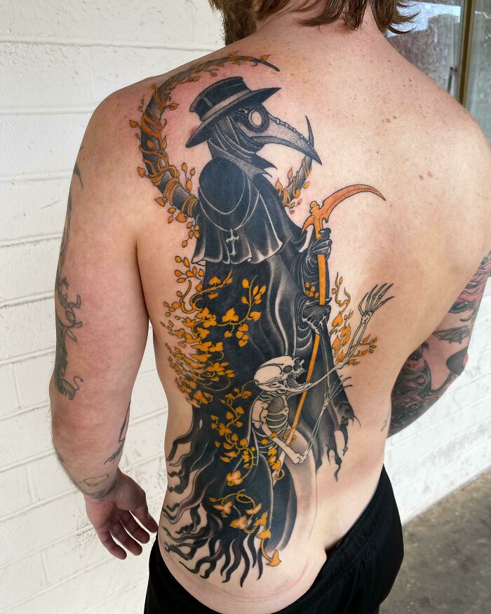 Back tattoo of a dark plague doctor with a scythe and orange floral accents, showcasing cool tattoos without regrets.