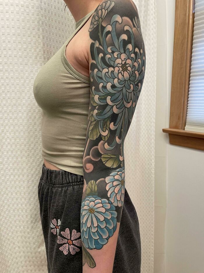 Full sleeve floral tattoo in blue and green tones on a person's arm showcasing cool tattoos without regrets.
