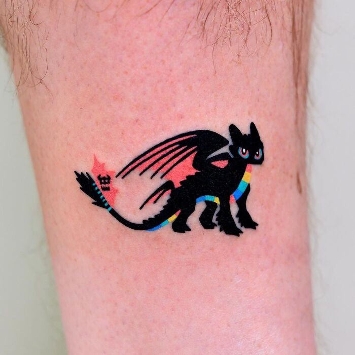 Small black dragon tattoo with colorful accents on a person's arm, showcasing one of the cool tattoos without regrets.