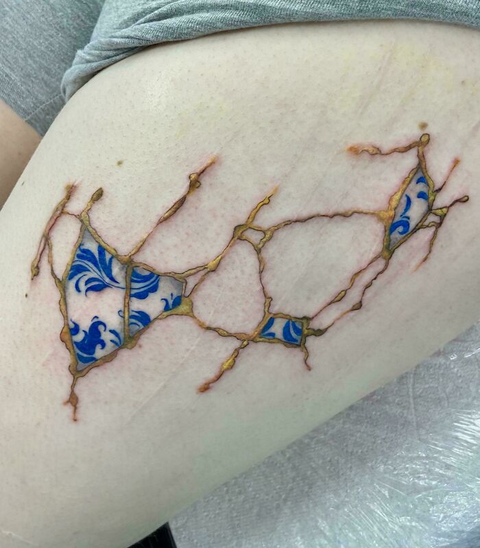 Abstract tattoo on skin with blue floral patterns and gold cracks, showcasing a cool tattoo design without regrets.