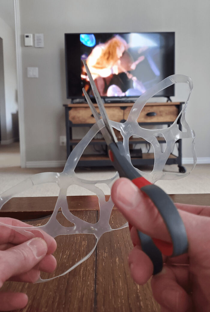 Hands using scissors to cut a plastic six-pack ring, nostalgic and relatable Gen X lifestyle moment in a living room.