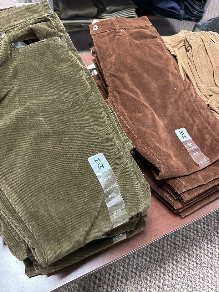 Stacks of green and brown corduroy pants folded on display, evoking nostalgic Gen X fashion styles.