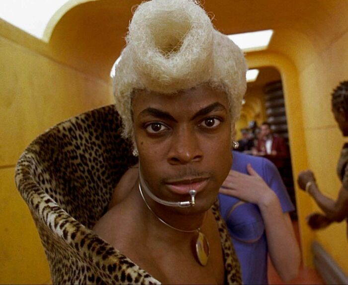 Close-up of a man with a unique blonde hairstyle and leopard print coat, evoking nostalgic Gen X cultural vibes.