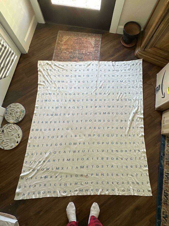 Large word search blanket laid on wooden floor, showcasing perfectly camouflaged letters that might take ages to find.
