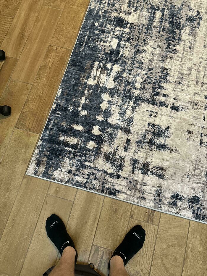 Person standing on wooden floor near a camouflaged patterned rug blending into the background.