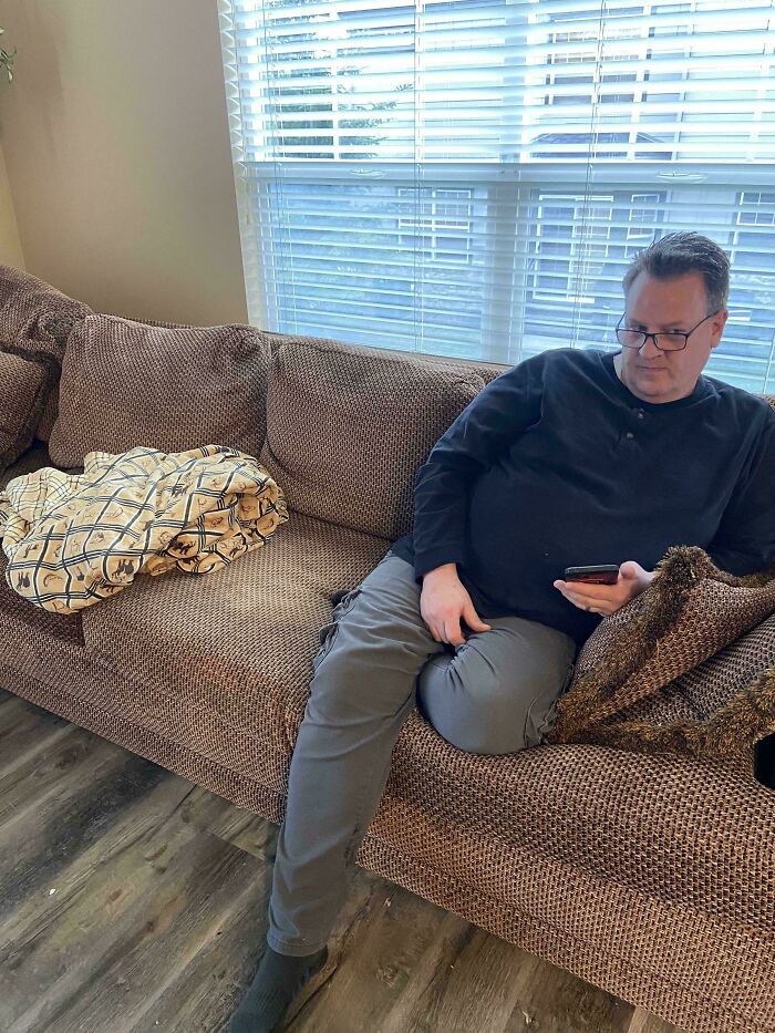 Man wearing glasses camouflaged on brown textured couch blending perfectly with the surroundings in a living room setting.