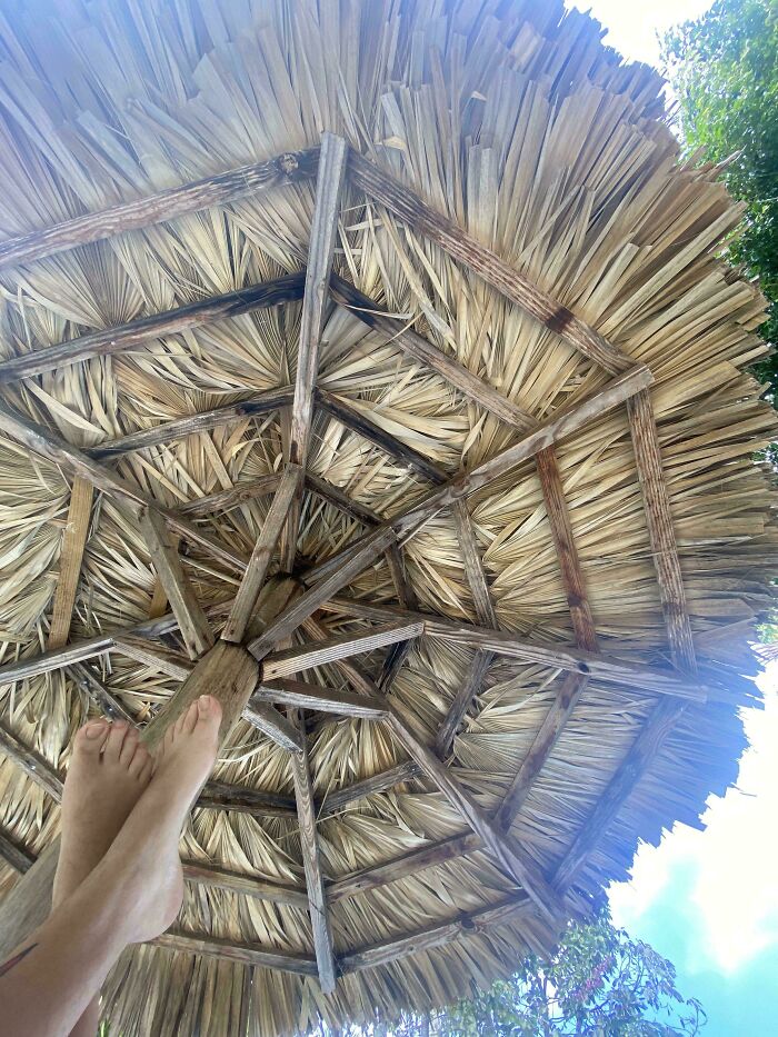 Feet resting under a camouflaged thatched umbrella blending with the natural background in a perfectly camouflaged scene.