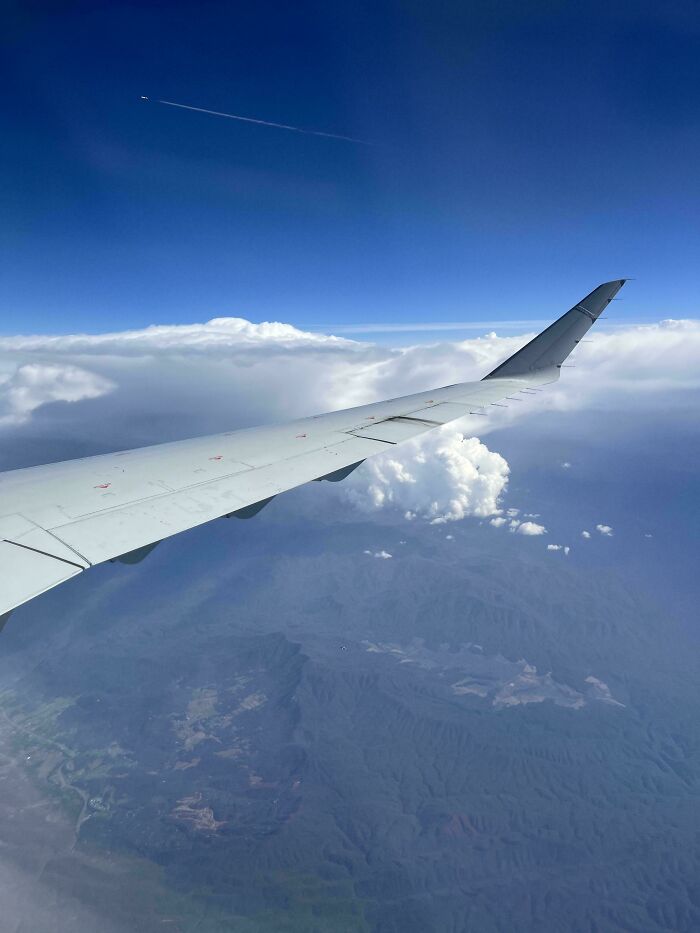 Airplane wing above mountains and clouds, showcasing a perfectly camouflaged plane wing blending into the sky.