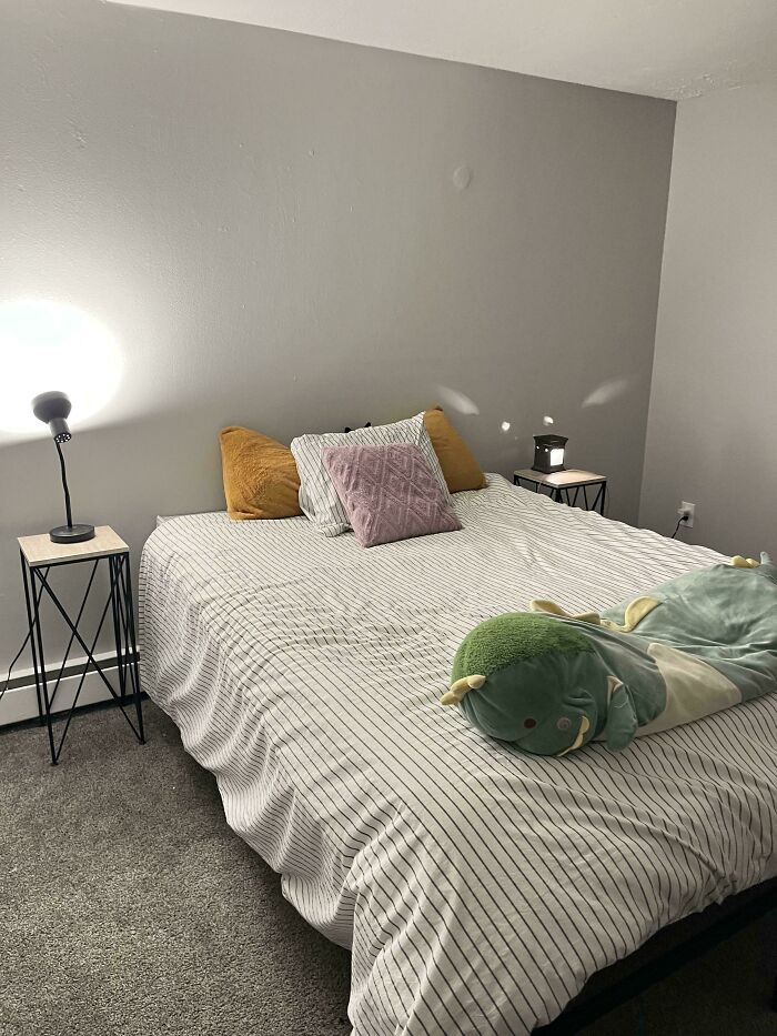 Cozy bedroom with striped bedding featuring perfectly camouflaged green plush toy blending into the bed linens and pillows.