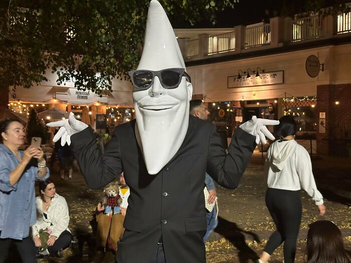 Person dressed as the Cool Spot mascot from the ’90s wearing black sunglasses and a suit at a nighttime outdoor event.