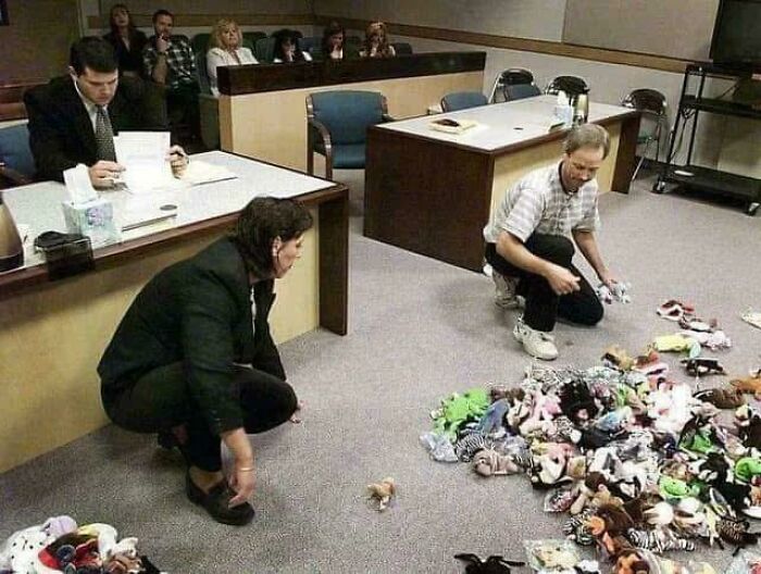 Two people sorting a large collection of nostalgic ’90s toys on a courtroom floor with spectators watching.