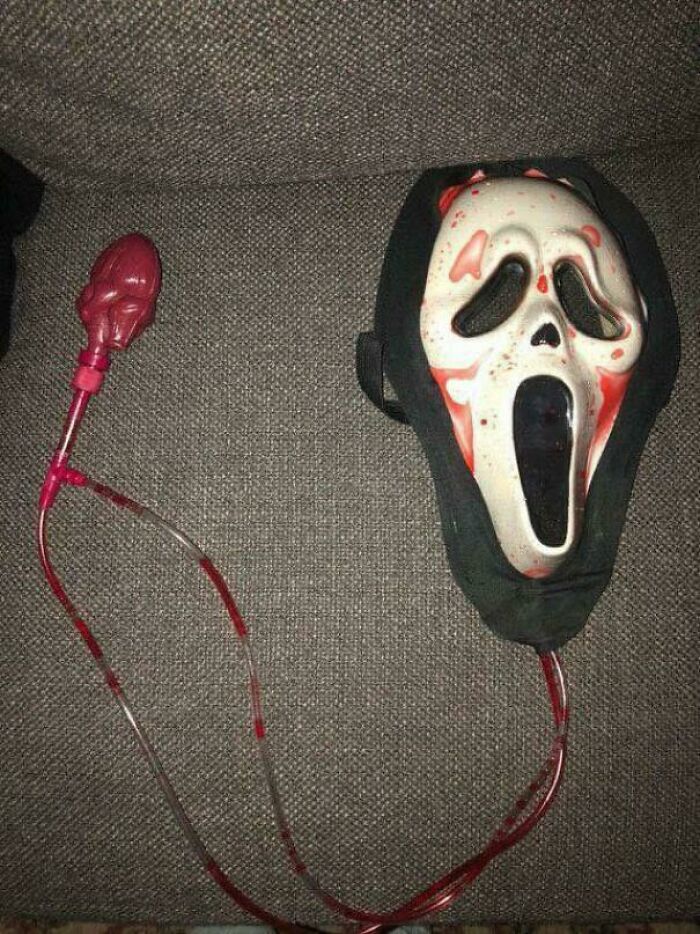 90s nostalgic Scream mask phone with blood-red cord resting on a gray fabric surface recalling kids today memories.