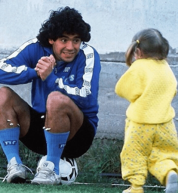 Soccer player kneeling smiling at little girl in yellow outfit on grass