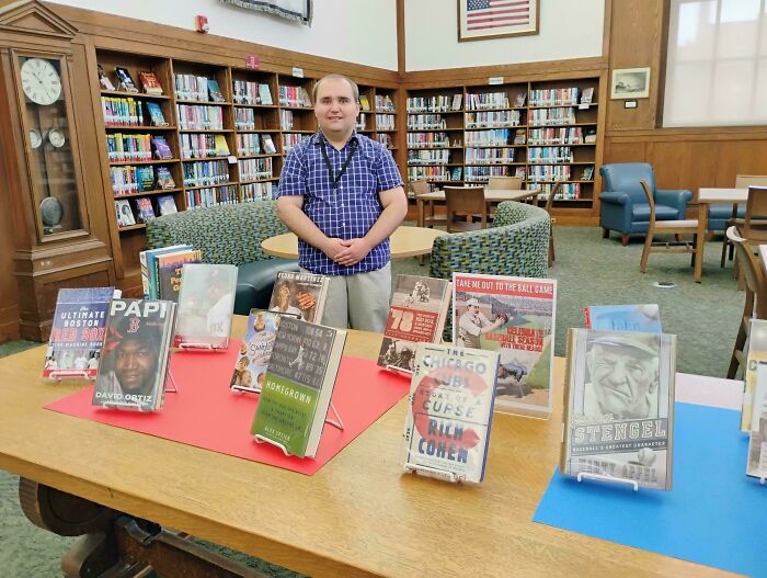 Man standing behind baseball books display in library with bookshelves