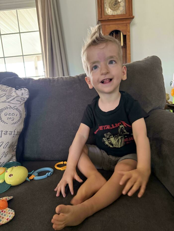 Happy young boy with blonde mohawk sitting on sofa with toys in living room