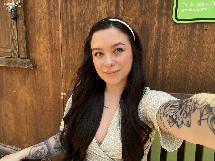 Young woman with long dark hair and floral tattoo taking selfie outdoors