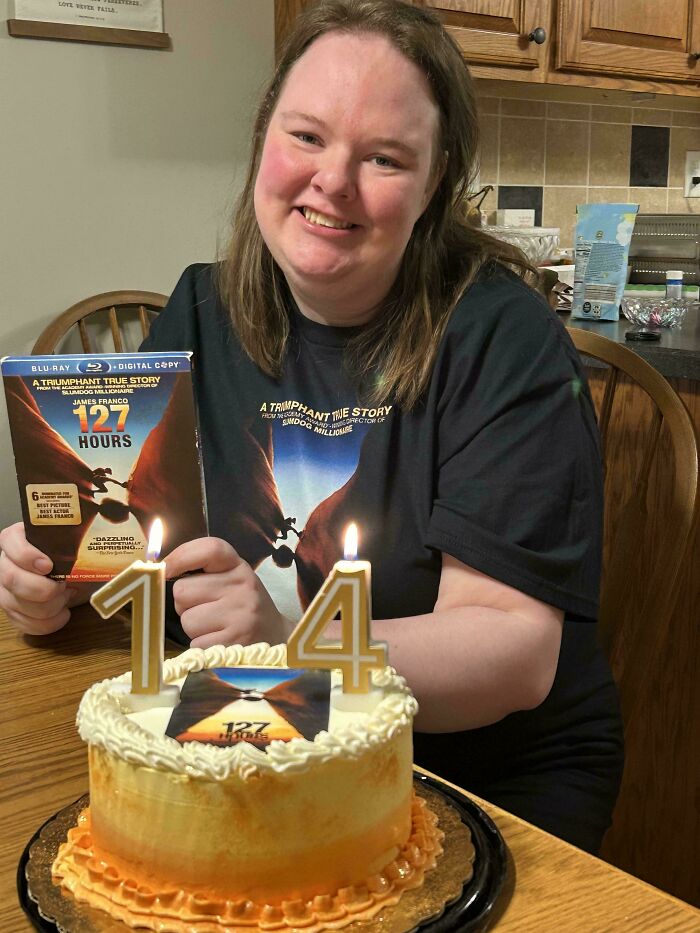 Smiling person celebrating birthday with 127 Hours themed cake and DVD