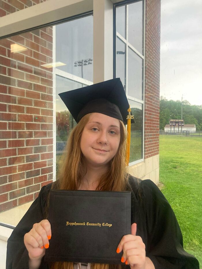 Graduate in cap and gown holding diploma from community college celebrating achievement