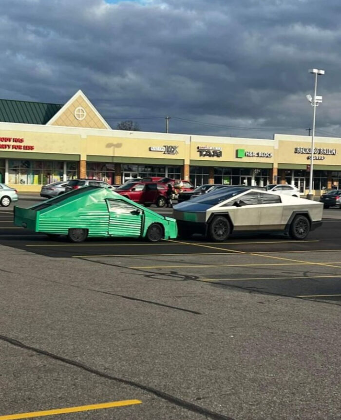 Two cars in a parking lot, one a handmade green vehicle and the other a futuristic gray Cybertruck style car, weird image.