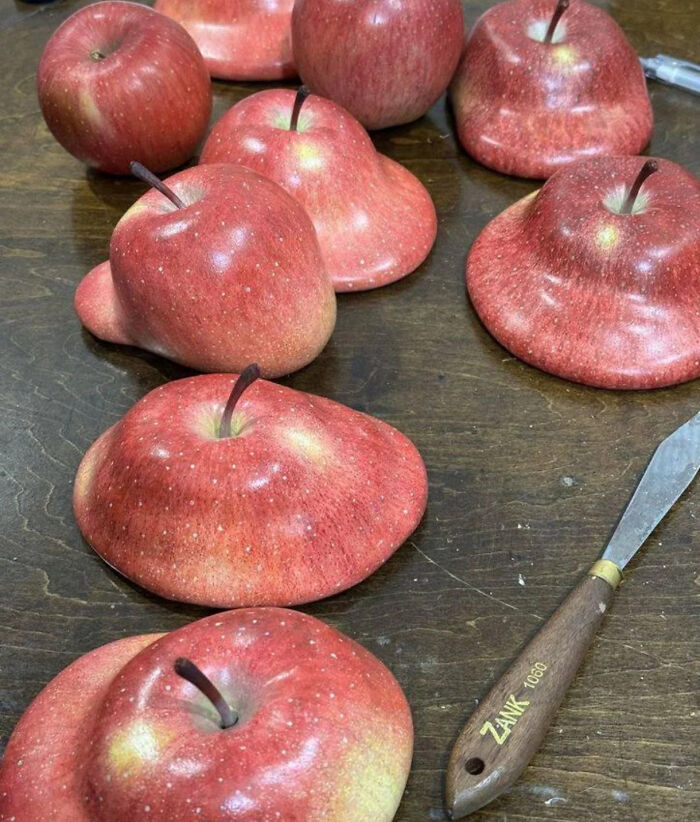 Red apples with distorted, flattened shapes arranged on a table, creating a weird and confusing cursed image.
