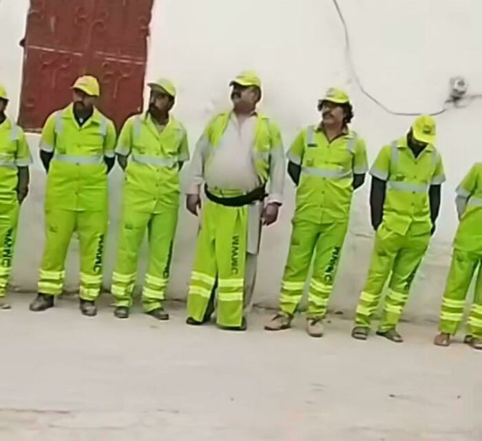Workers wearing bright yellow uniforms with reflective stripes standing in a row showcasing weird and confusing visual details.