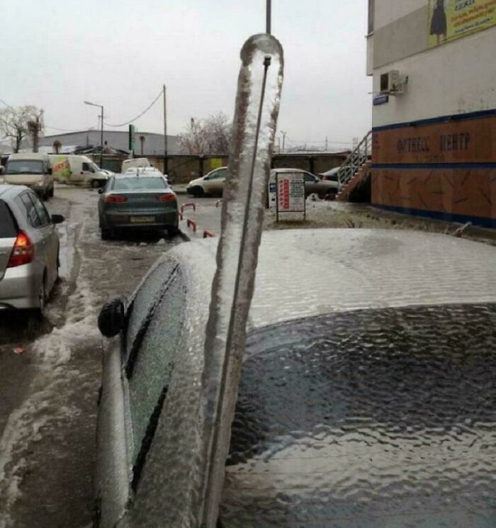 Car covered in thick ice with a large icicle standing vertically, showcasing a weird and confusing frozen scene.