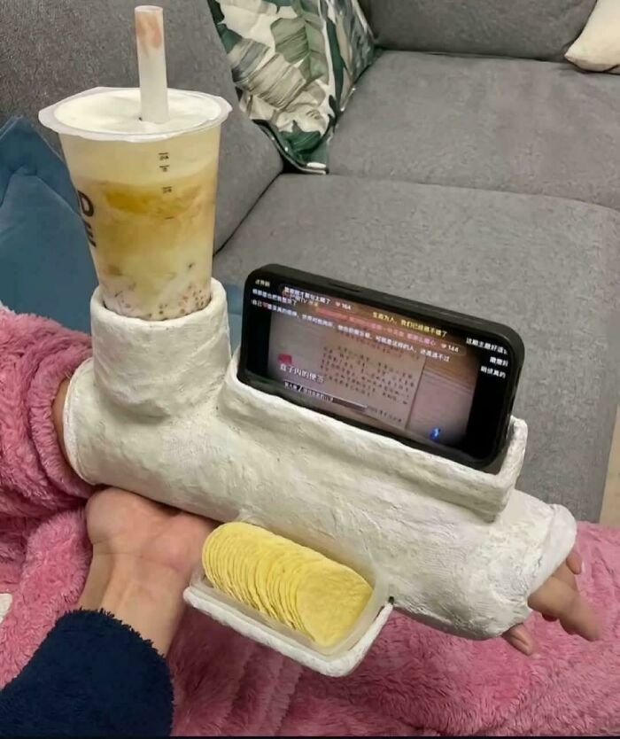 Unusual snack holder with phone stand and drink cup designed for hands-free use on a couch.
