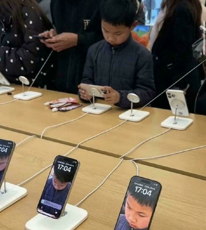 Boy playing on phone in a store with multiple phones displaying his face, a weird and confusing cursed image.