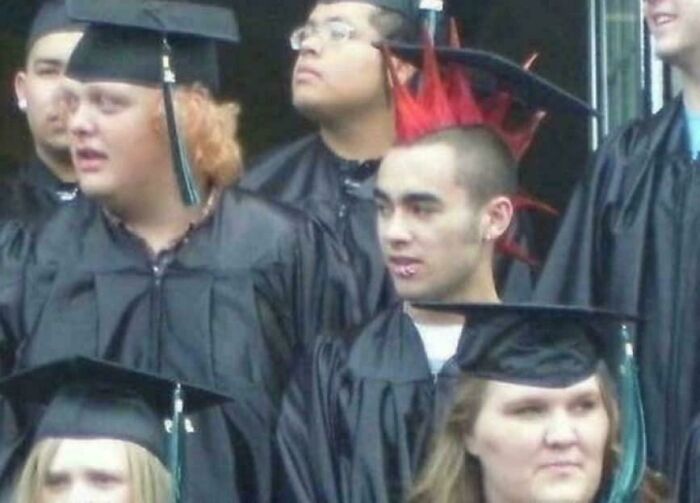 Group of graduates in caps and gowns, with one wearing red spiked hair, a weird and confusing image.