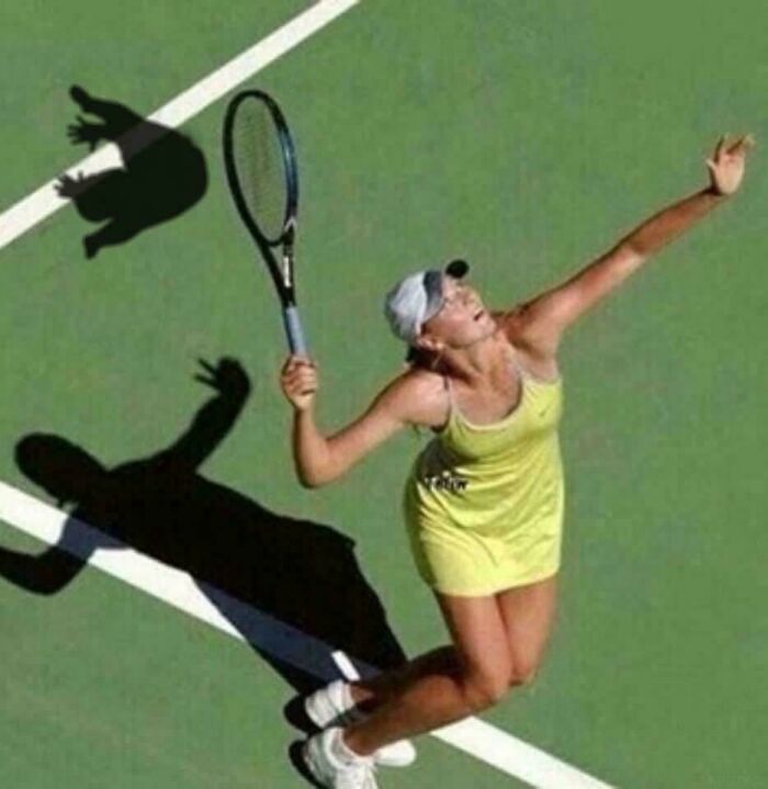 Tennis player serving on court with shadow creating a weird and confusing visual effect.