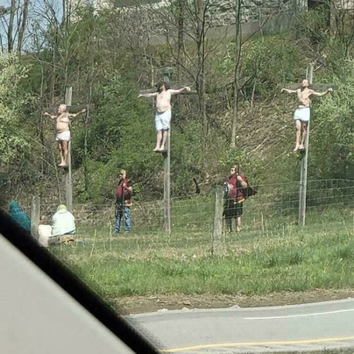 Three people posed on crosses in a confusing outdoor scene with bystanders nearby, creating a weird and cursed image.