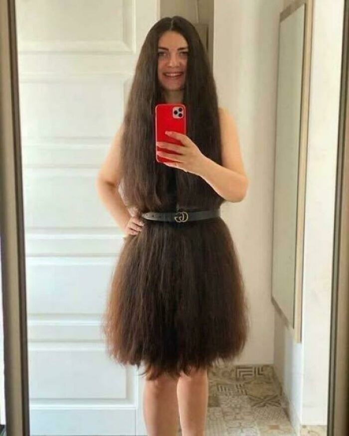 Woman taking a mirror selfie wearing her long hair styled as a dress with a belt in a confusing and weird image.