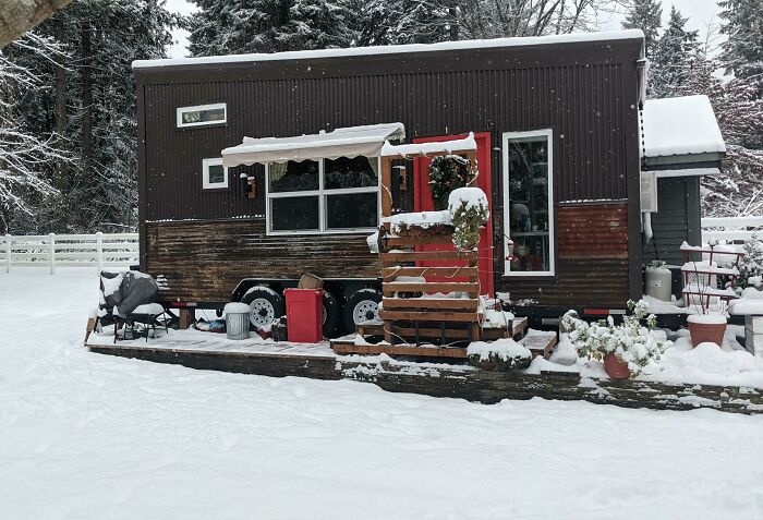Snow-covered tiny house with rustic exterior and outdoor seating