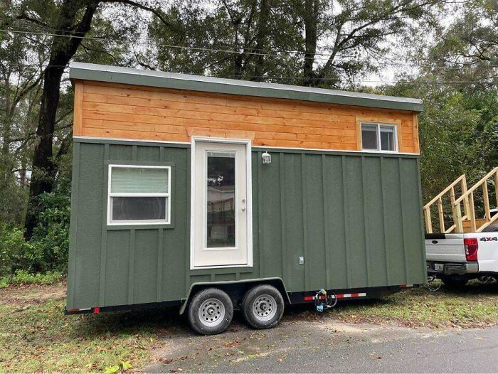 Green and wood tiny house on wheels parked beside a truck on road