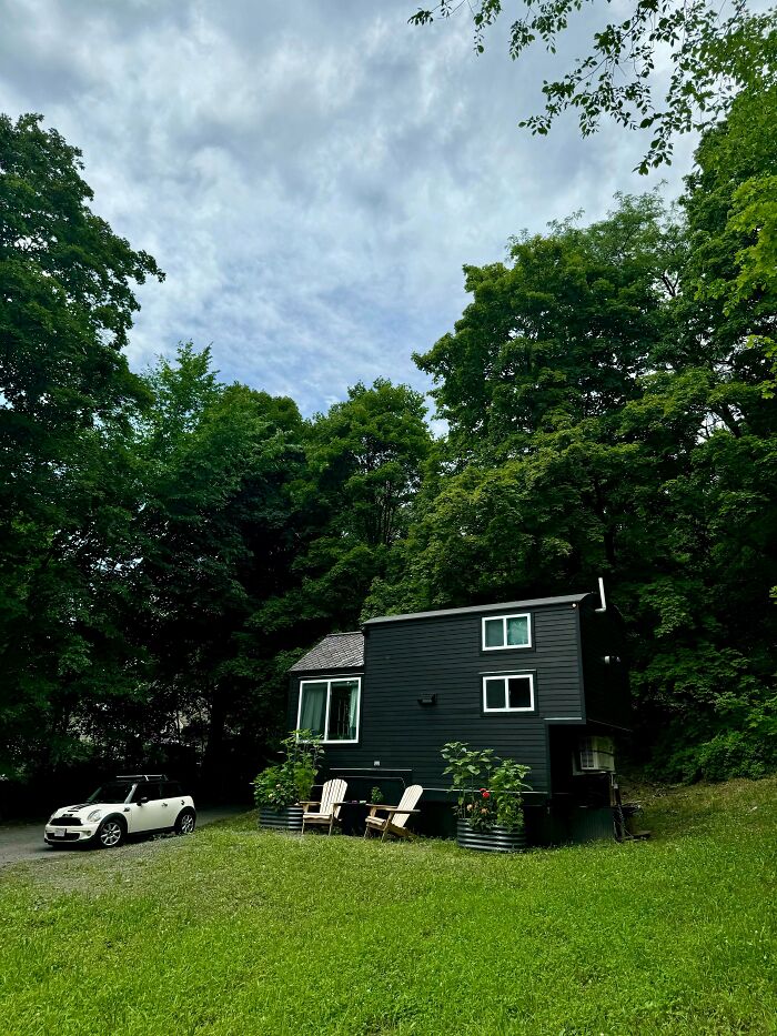 Black small home with multiple windows near green trees and white car