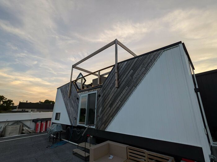 Modern tiny home with rooftop deck and wooden siding under cloudy sky
