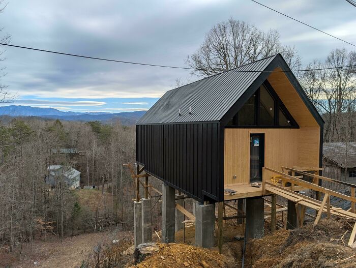 Black and wood tiny home elevated on pillars with mountain views