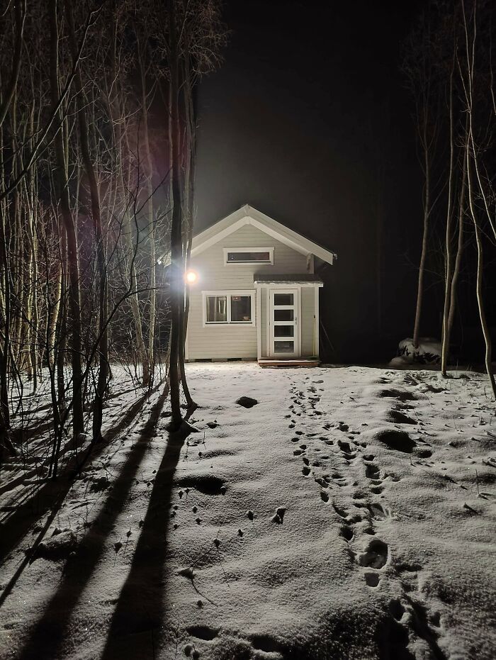 Tiny white house illuminated at night with snow and tree shadows