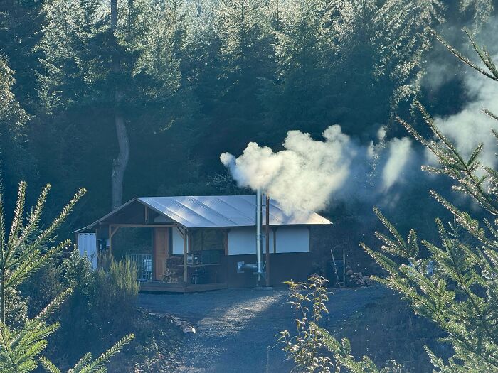 Compact cabin with smoke from chimney nestled in forest