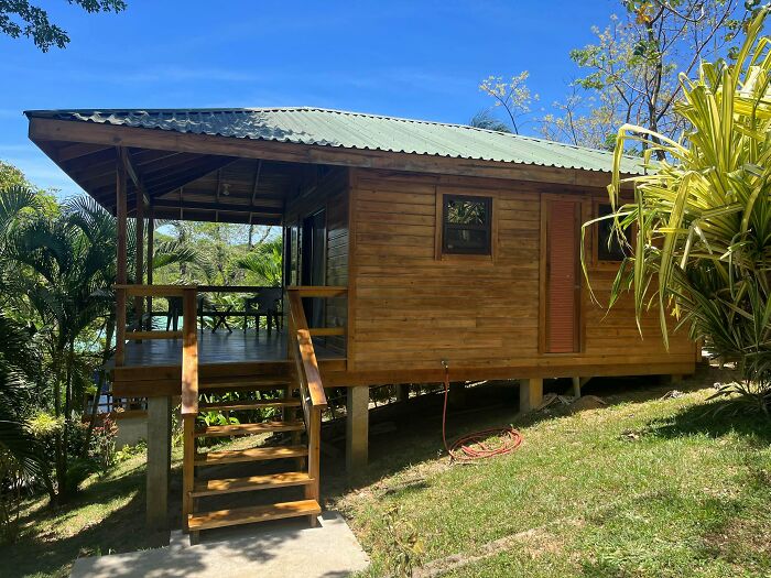 Small wooden home with covered porch surrounded by greenery